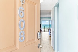 A door with numbers 6068, a keypad lock, and a view of a balcony with a chair and a table.