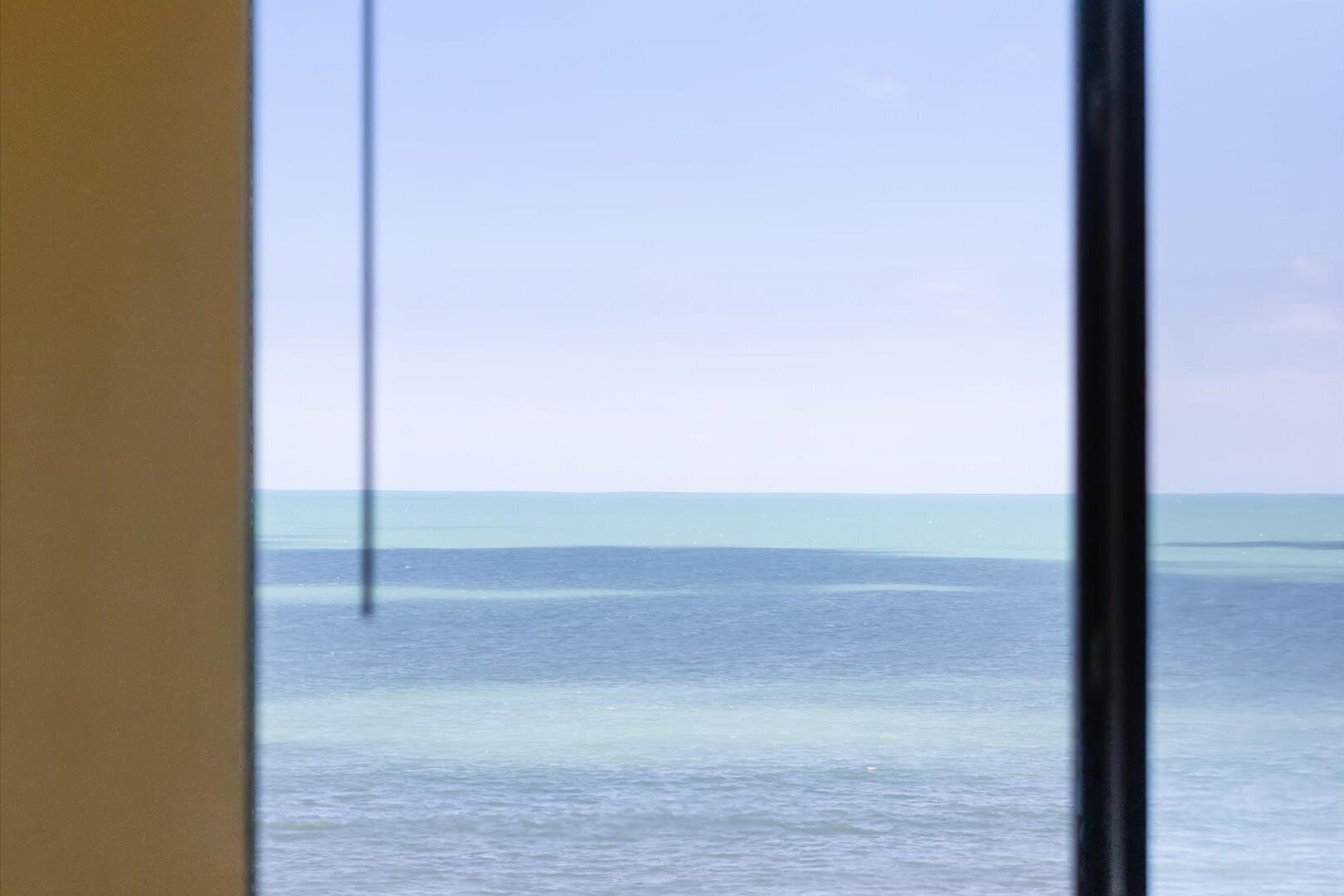 A view through a window with a clear sky and calm sea.