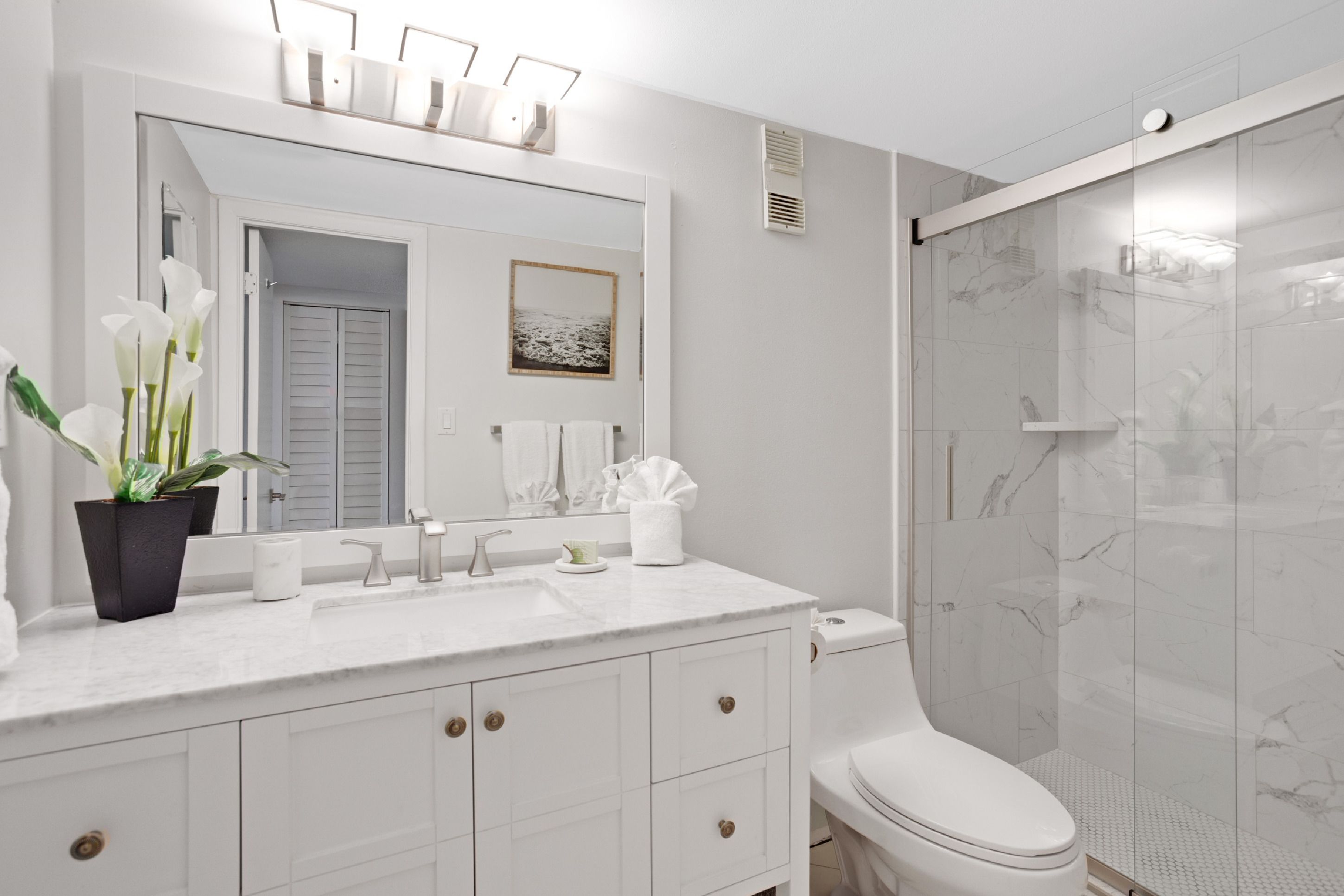 Une salle de bain moderne avec un meuble-lavabo blanc, un grand miroir, des toilettes et une douche à parois de verre.