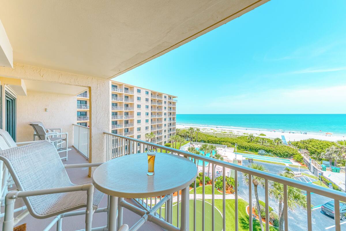 A balcony with a table and chairs, overlooking a beach and a resort area.