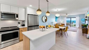 A modern kitchen with white cabinets, stainless steel appliances, and a central island with a bowl of bread. - Canaveral Towers - Oceanfront Condos with Pool and Mini Golf by Port Canaveral - Cocoa Beach (Cape Canaveral)