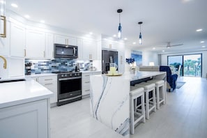 A modern kitchen with white cabinets, a central island, stainless steel appliances, and pendant lighting.