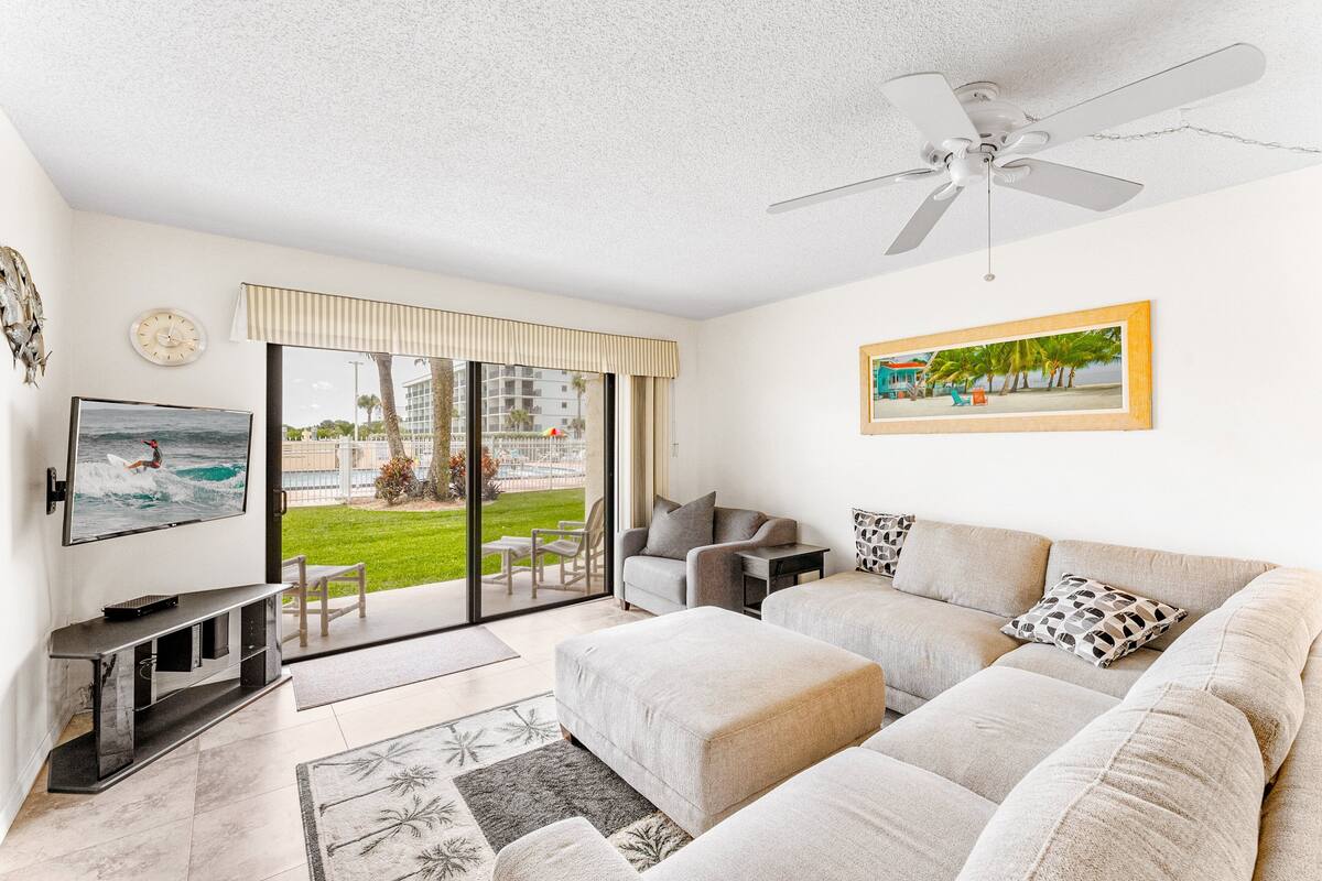 A living room with a TV, sofa, and a view of a beach.