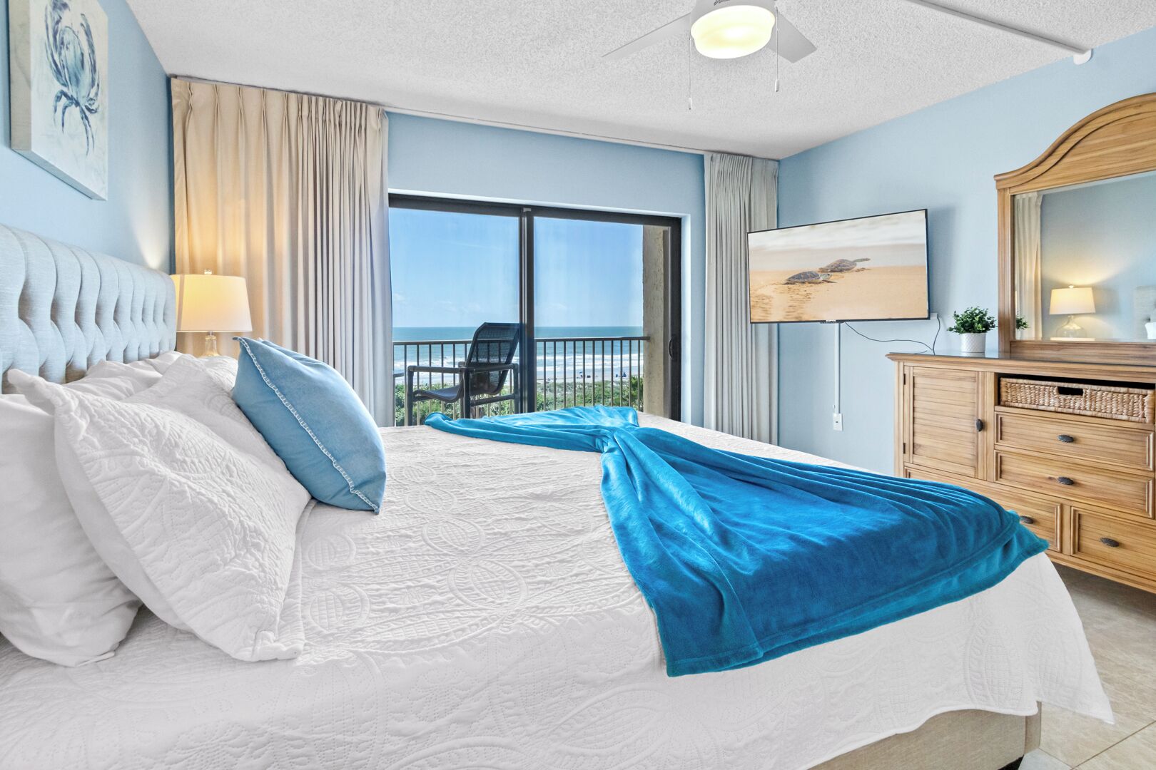Een hotelkamer met een groot bed, een balkon met uitzicht, een houten dressoir en een plafondventilator.