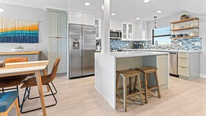 A modern kitchen with a central island, stainless steel appliances, and a dining area with a table and chairs. - Canaveral Towers - Oceanfront Condos with Pool and Mini Golf by Port Canaveral - Cocoa Beach (Cape Canaveral)