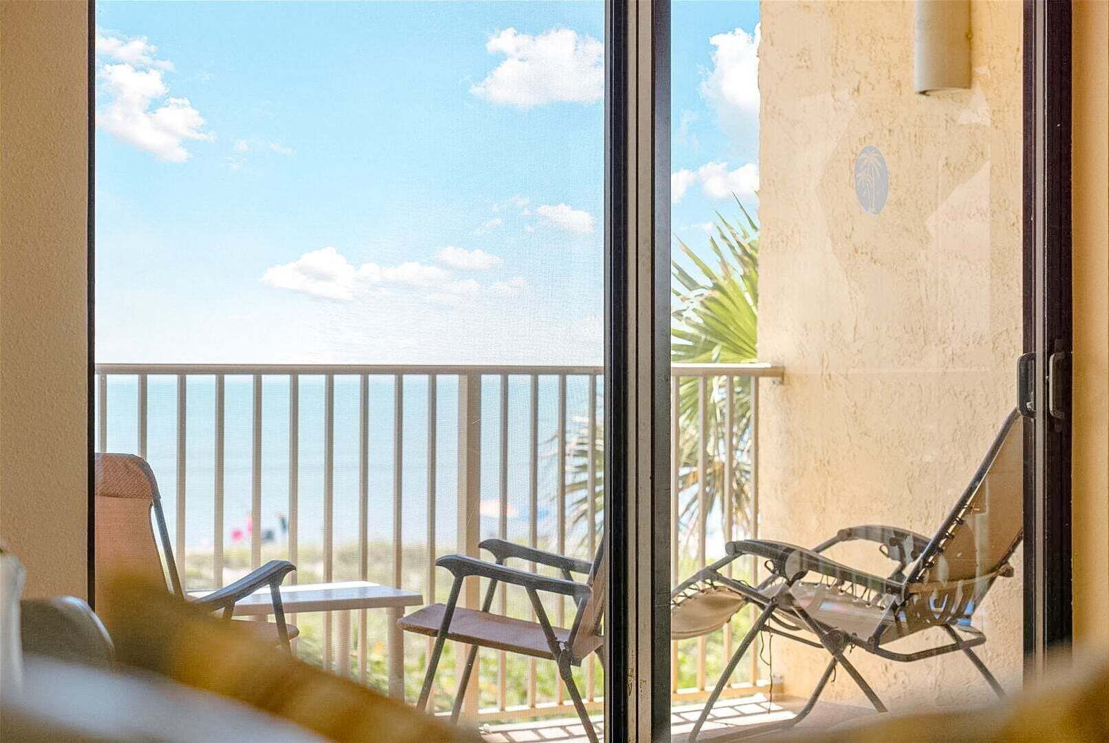 Een balkon met uitzicht op de oceaan, een palmboom en een stoel.