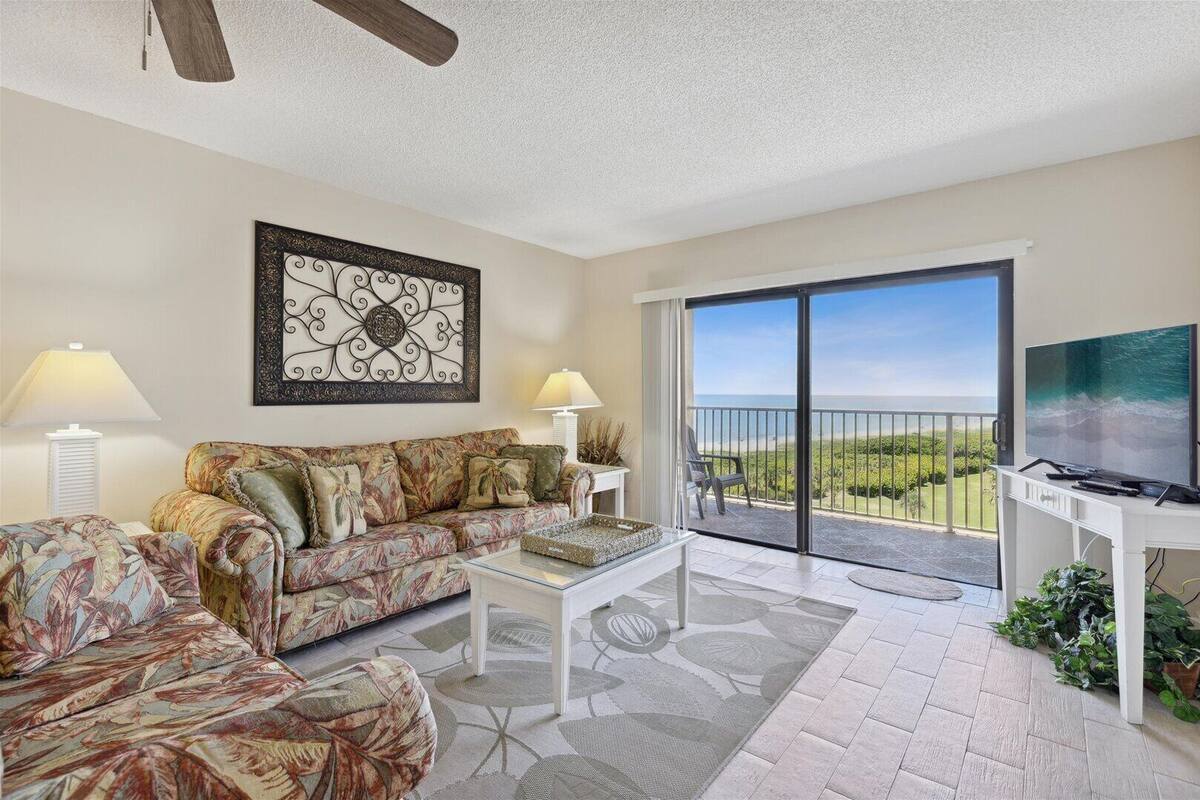 A living room with a sofa, coffee table, and a TV on a balcony with a view.