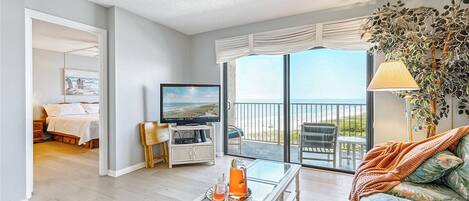 A spacious living area with a balcony, a television, and a view of the beach.