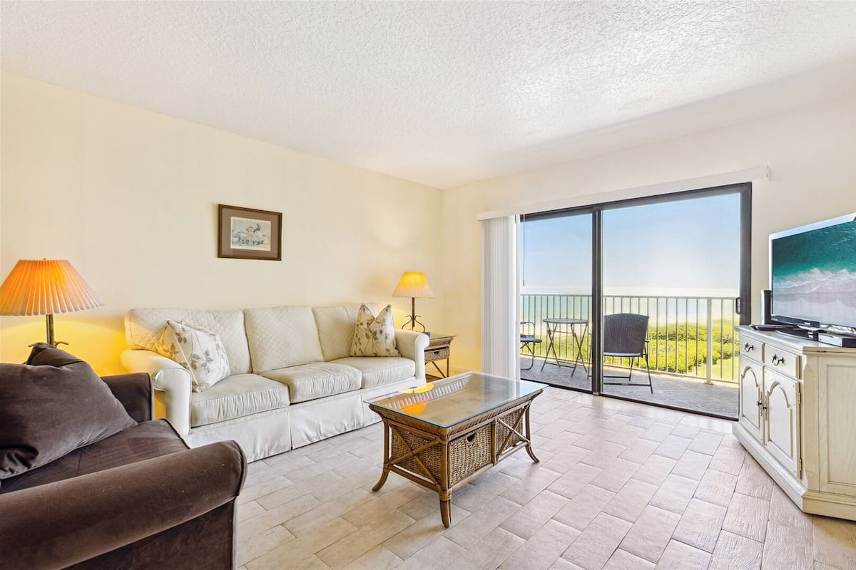 A living room with a sofa, a coffee table, and a TV on a balcony.