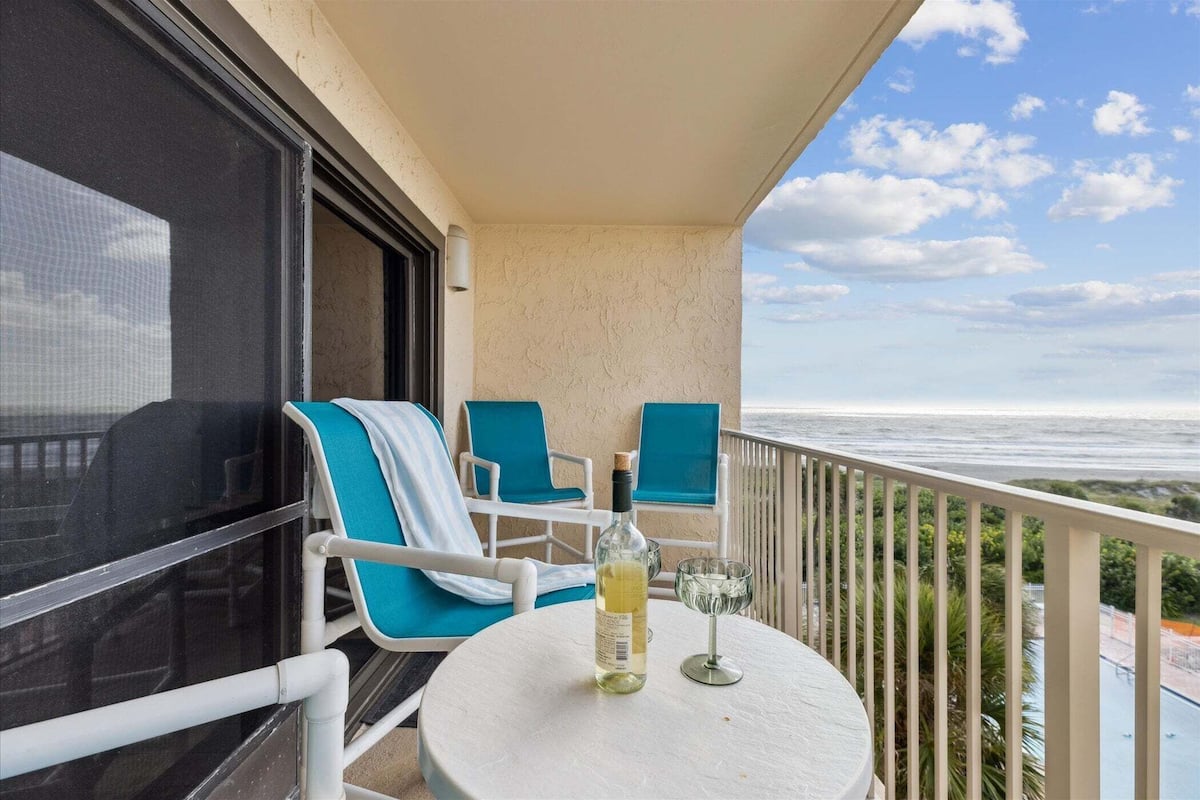 A balcony with a table, two chairs, a bottle, and a glass.