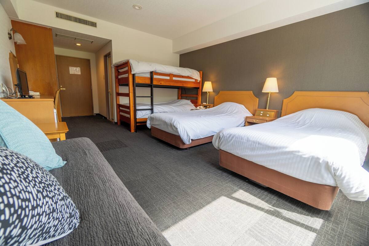 Habitació d'hotel amb dos llits individuals, un sofà, una taula de nit i un mirall.