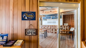 Un interior de madera con un letrero que dice 'Welcome Open', una zona de bar con taburetes de madera y una pizarra de menú.