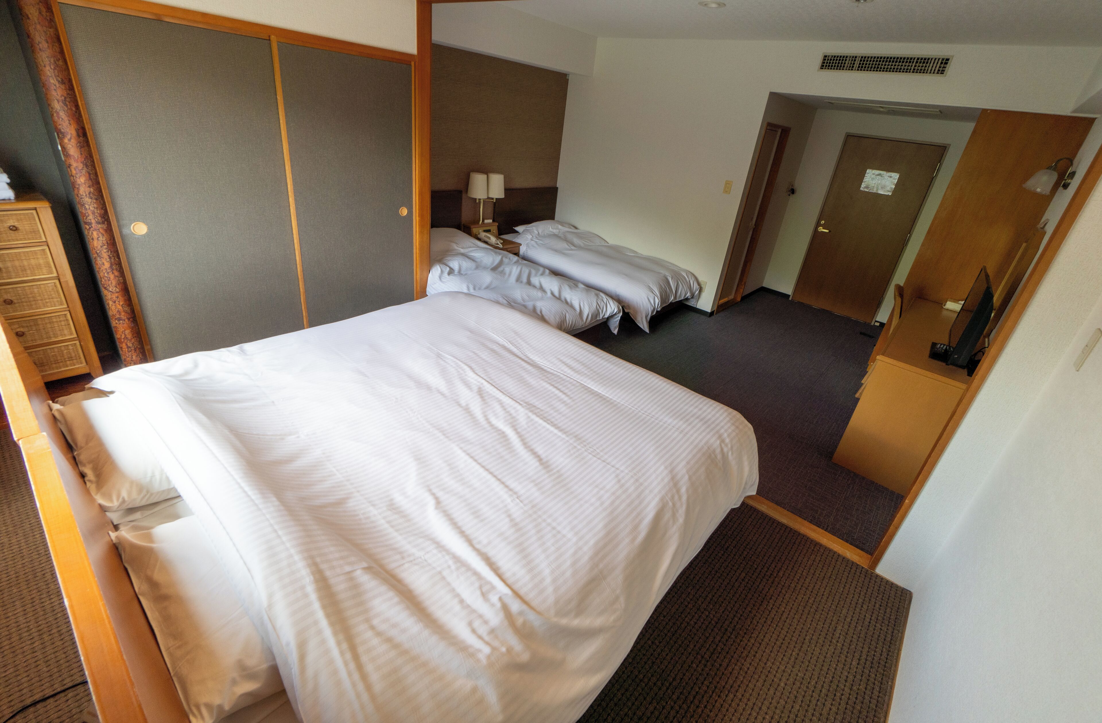 A hotel room with a large bed, a smaller bed, a desk, and a wardrobe.