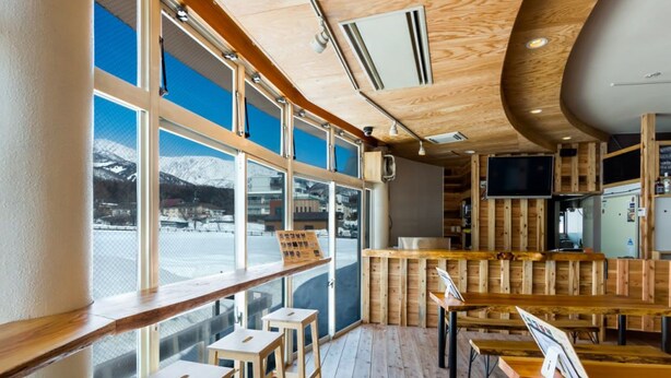 Un restaurante con interiores de madera, ventanas amplias y vistas a montañas nevadas.