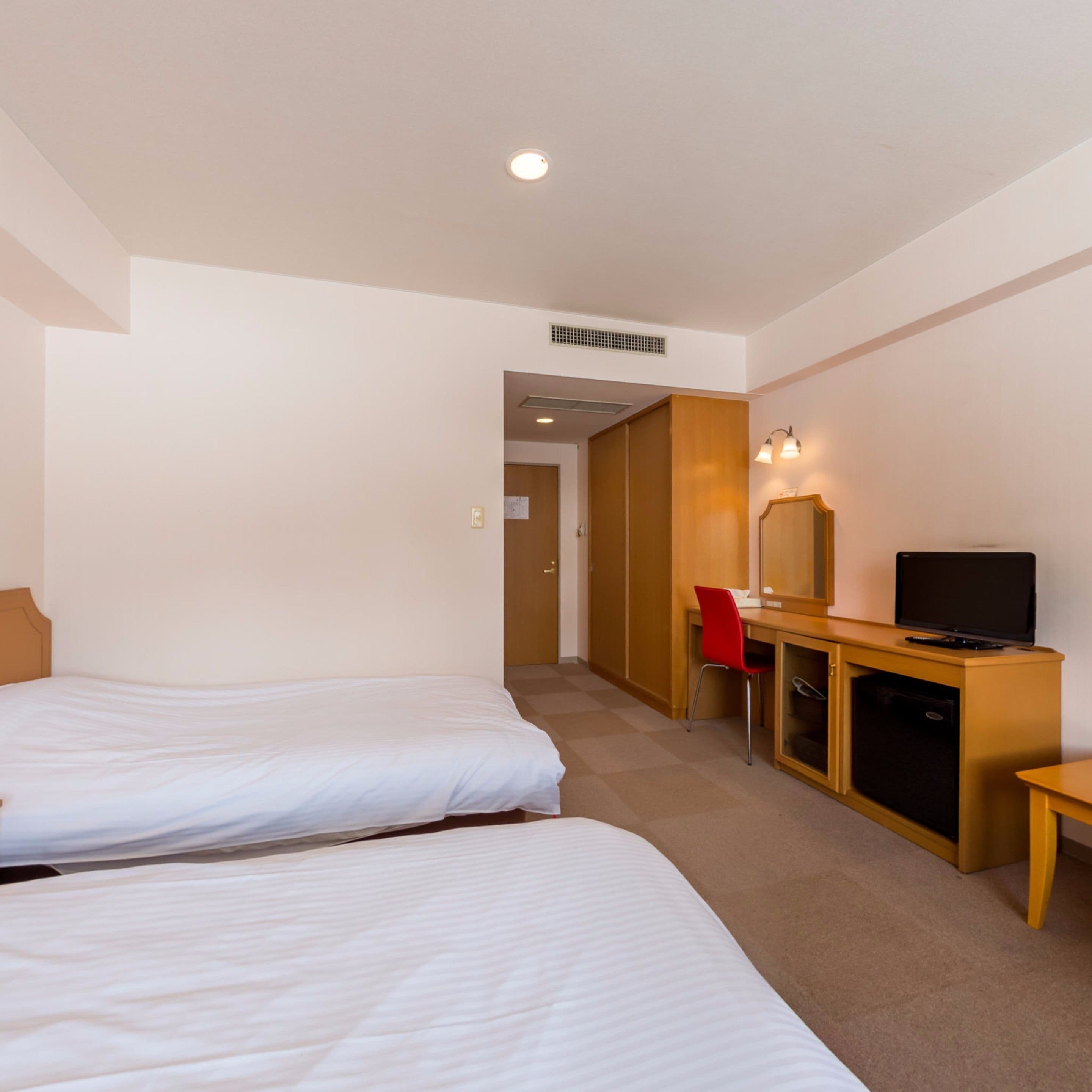 Habitación de hotel con dos camas, un escritorio con computadora y televisor, una silla y un armario.