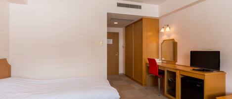 Habitación de hotel con dos camas, un escritorio con computadora y televisor, una silla y un armario.