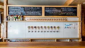 Zona de bar con mostrador de madera, múltiples grifos y una pizarra que muestra una variedad de cervezas y ales.