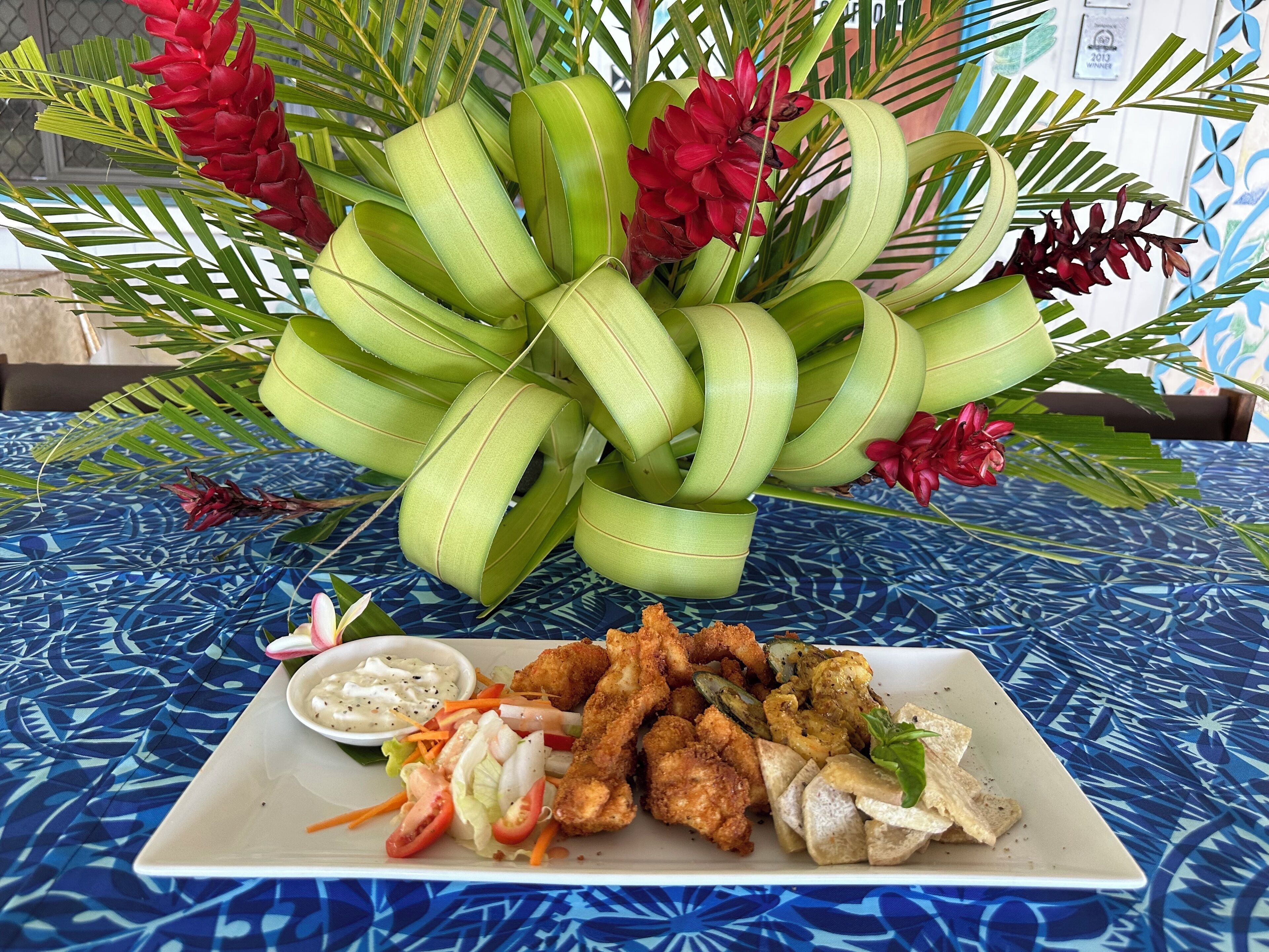 A table with a plate of fried food, a salad, and a decorative plant arrangement.