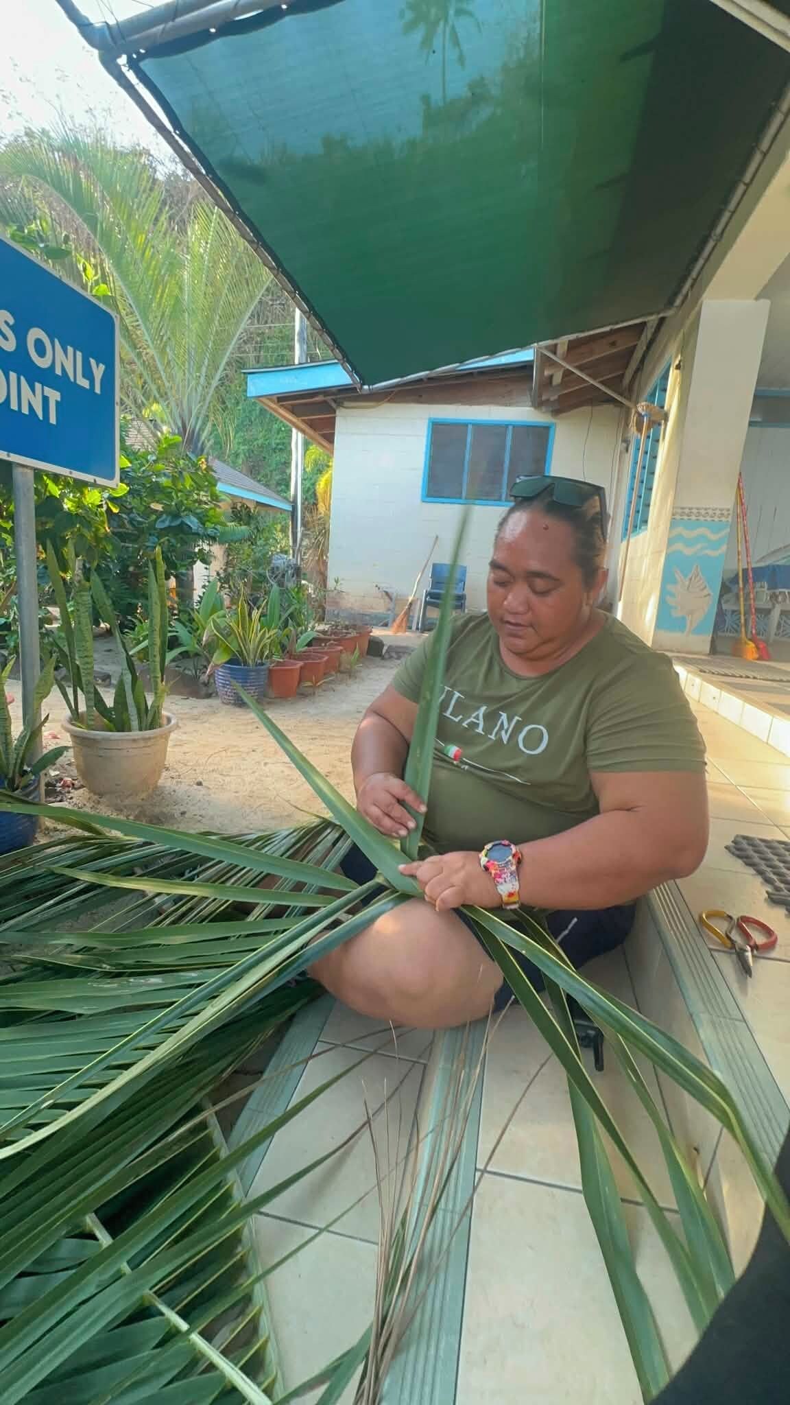 A person sitting on a bench with a pile of green leaves beside them.