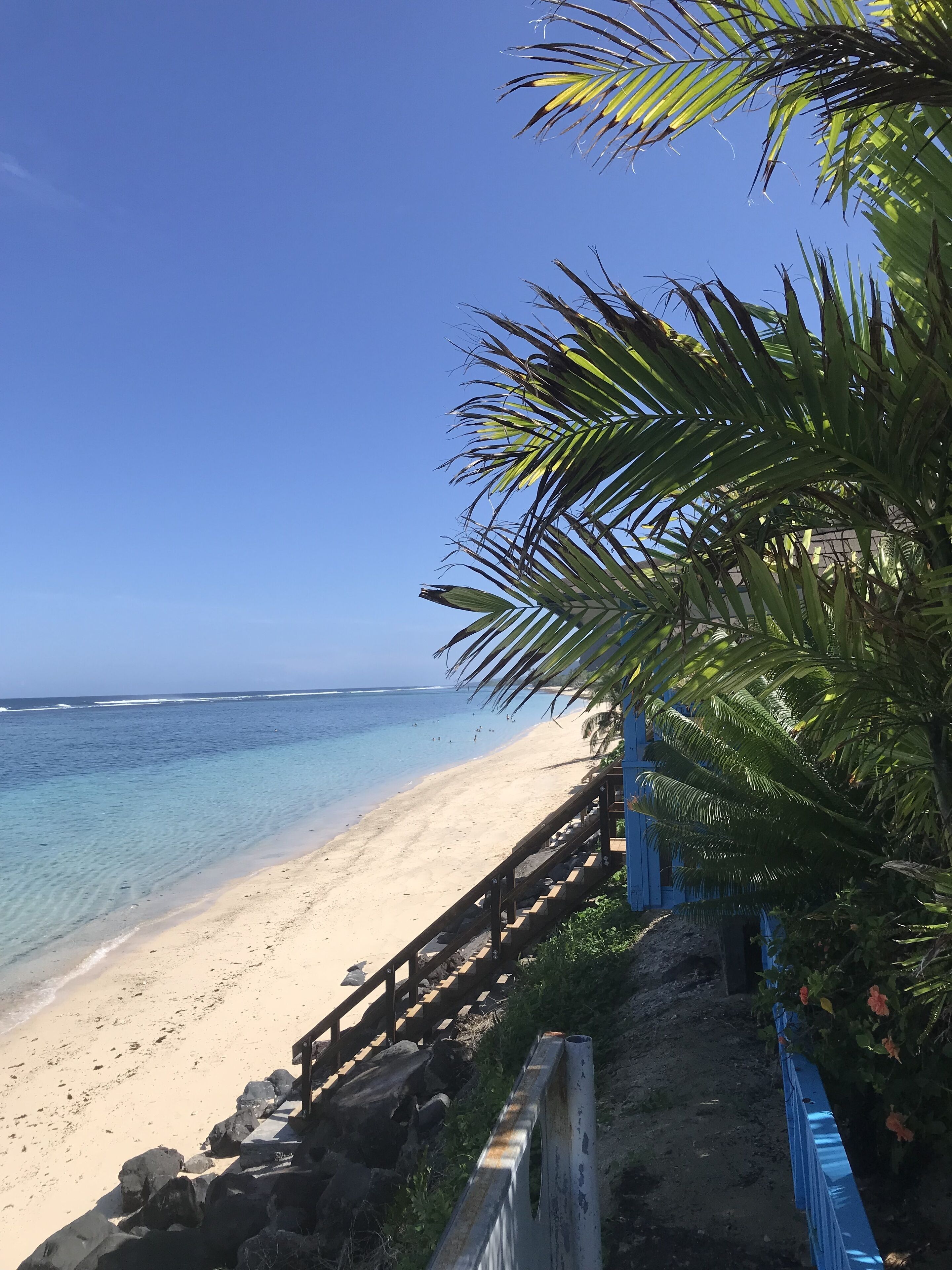 A beach with clear blue water, a sandy shore, and a wooden fence.