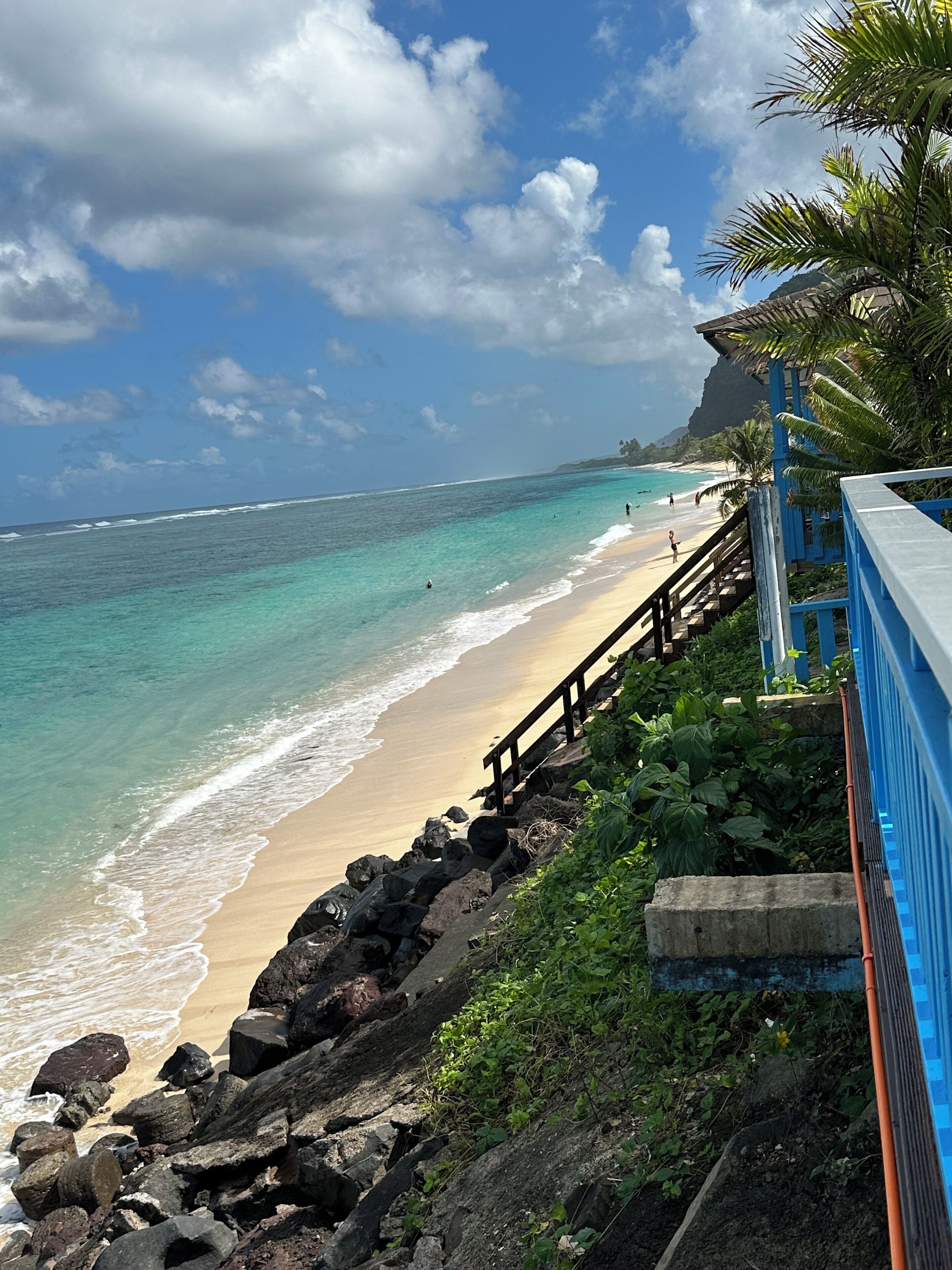Une plage aux eaux turquoise et limpides, une promenade en bois et une côte rocheuse.