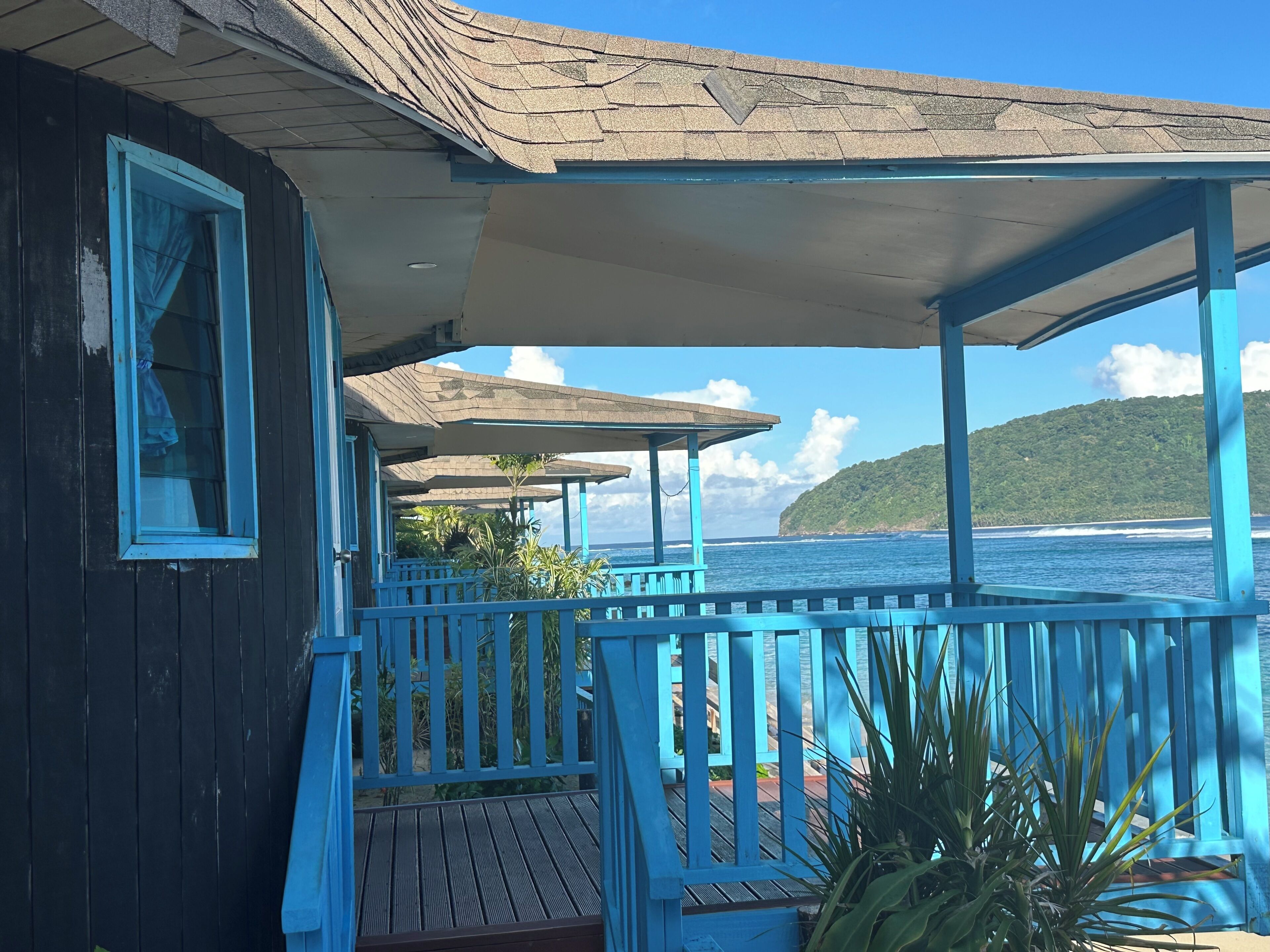 A covered outdoor area with a wooden deck, a railing, and a view of the ocean.