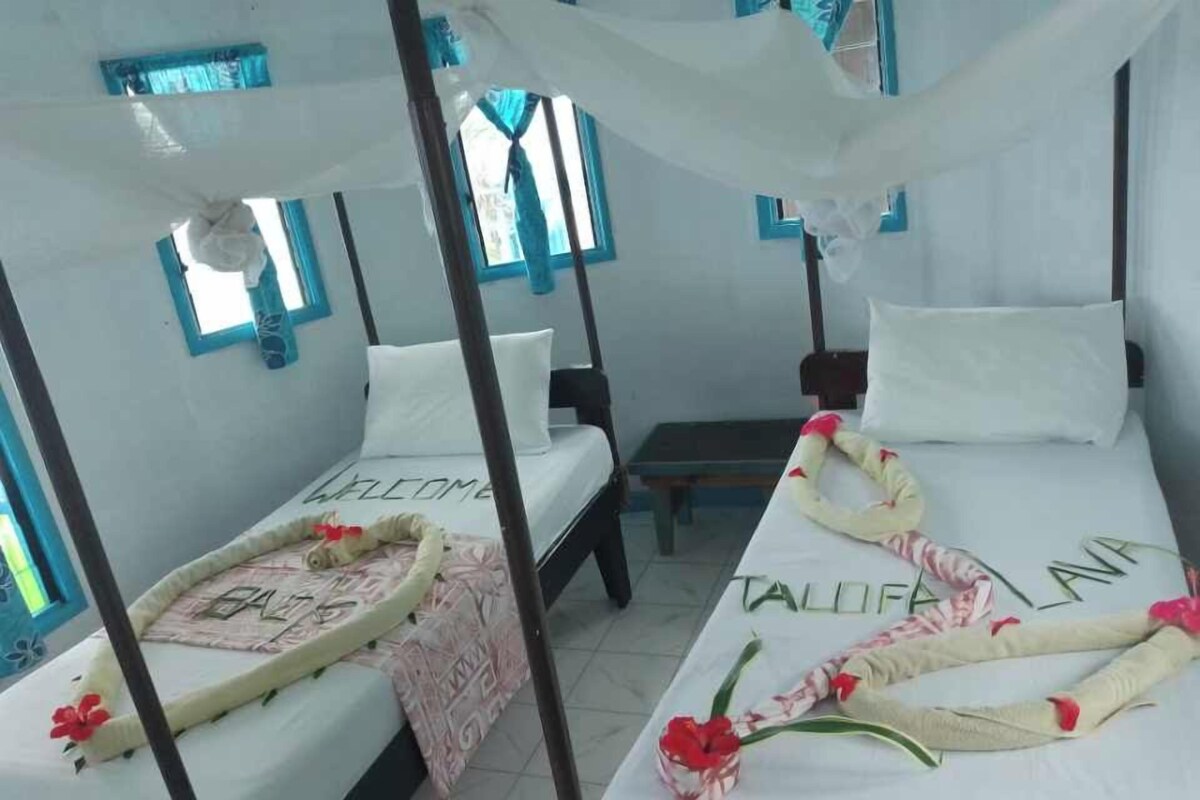 A room with two beds, each with a canopy, and a bench. The beds have decorative pillows and a welcome mat.