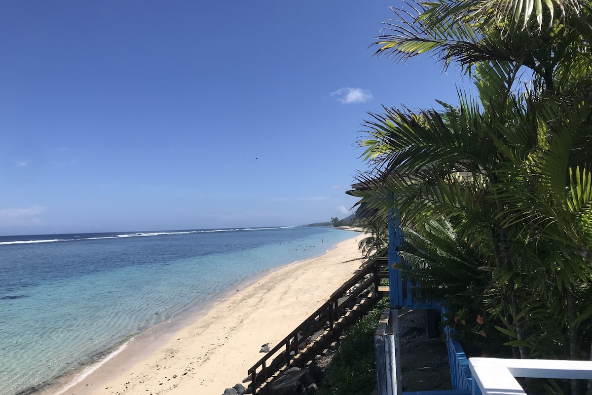 Ein Strand mit klarem türkisblauem Wasser, einem Sandstrand und einer Holzpromenade, die zum Strand führt.