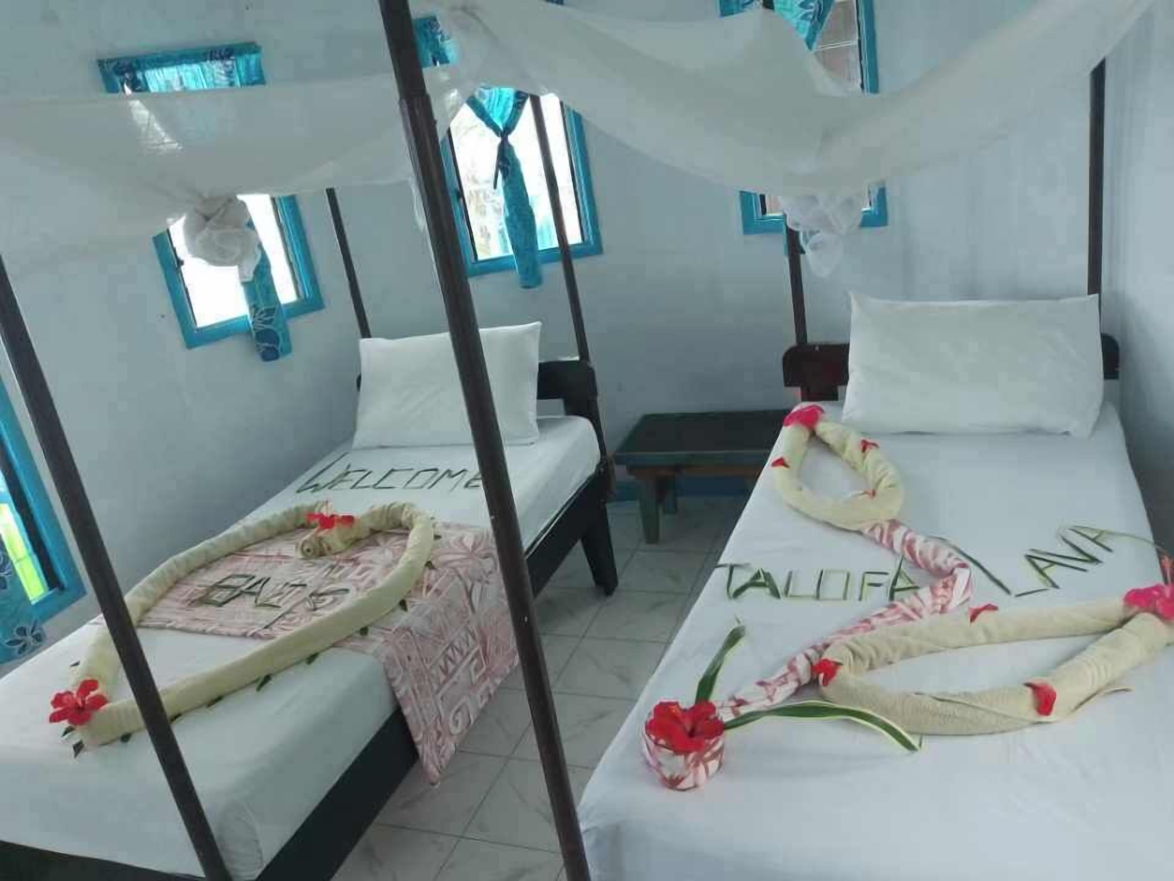 Une chambre avec deux lits, chacun doté d’un baldaquin, et un banc. Les lits sont agrémentés d’oreillers décoratifs et un tapis d’accueil est posé à l’entrée.