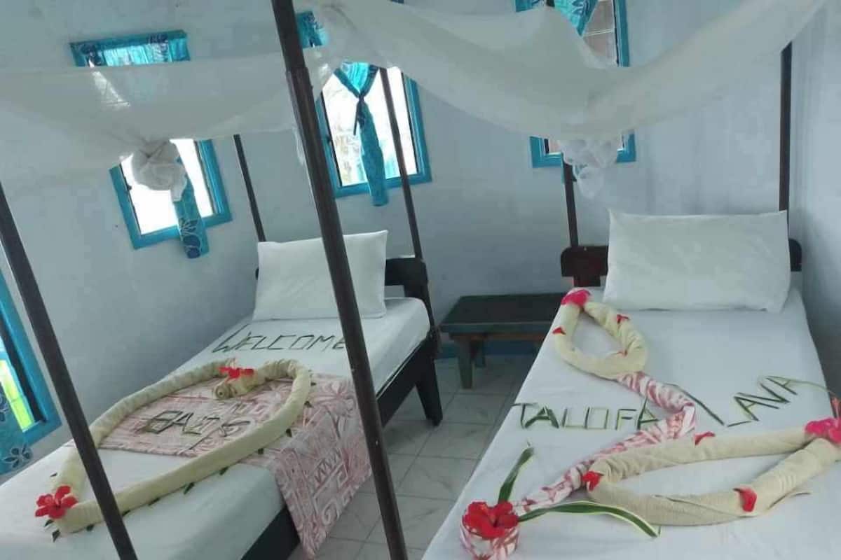 Ein Zimmer mit zwei Betten, jeweils mit Baldachin, und einer Bank. Die Betten sind mit dekorativen Kissen und einer Willkommensmatte ausgestattet.