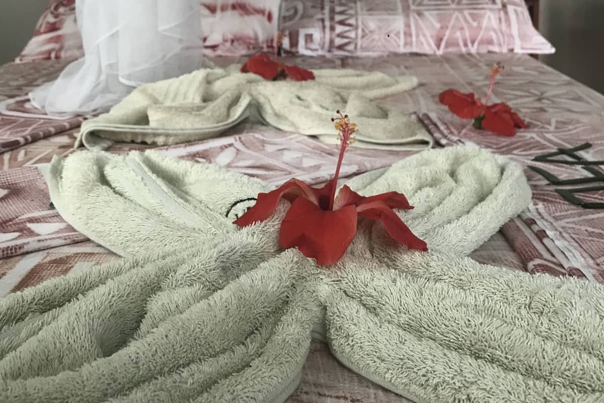 Ein Bett mit einem gemusterten Bettüberwurf, einem weißen Moschee-Vorhang und einer roten Blumenarragemment.