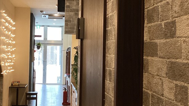 A hallway with a brick wall, a wooden door, and a seating area with orange chairs. - Osaka Namba Hostel MIYABI (Osaka)