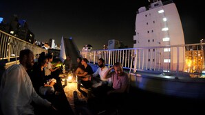 A group of people seated on a rooftop terrace with a railing, overlooking a cityscape at night. - Osaka Namba Hostel MIYABI (Osaka)