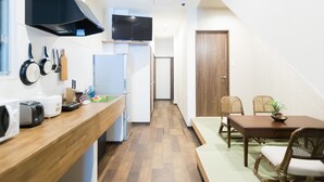 A compact kitchen with a wooden countertop, a microwave, a toaster, and a sink. There is a dining area with a table and chairs, and a television mounted above the counter. - Osaka Namba Hostel MIYABI (Osaka)