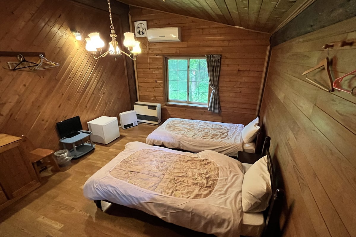 A cozy cabin room with two beds, a desk, a chair, a television, and a window with curtains.