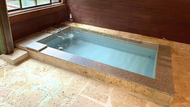 Een rechthoekig whirlpoolbad met een heldere waterfunctie, geplaatst tegen een houten wand met een raam erboven.