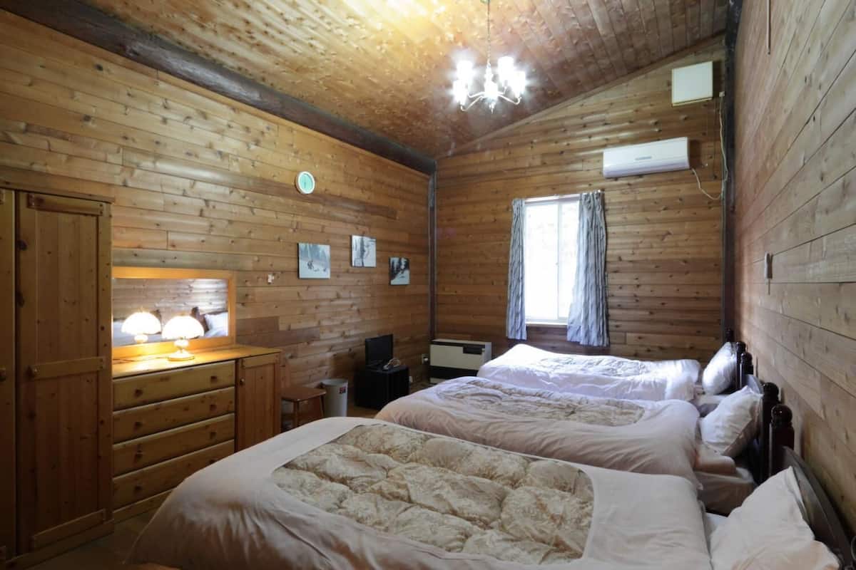 A wooden-paneled room with two beds, a desk with a lamp, a television, and a window with curtains.