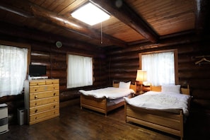 A log cabin room with two wooden beds, a dresser, a television, and a ceiling light. - Canadian Village Goryu (Hakuba)