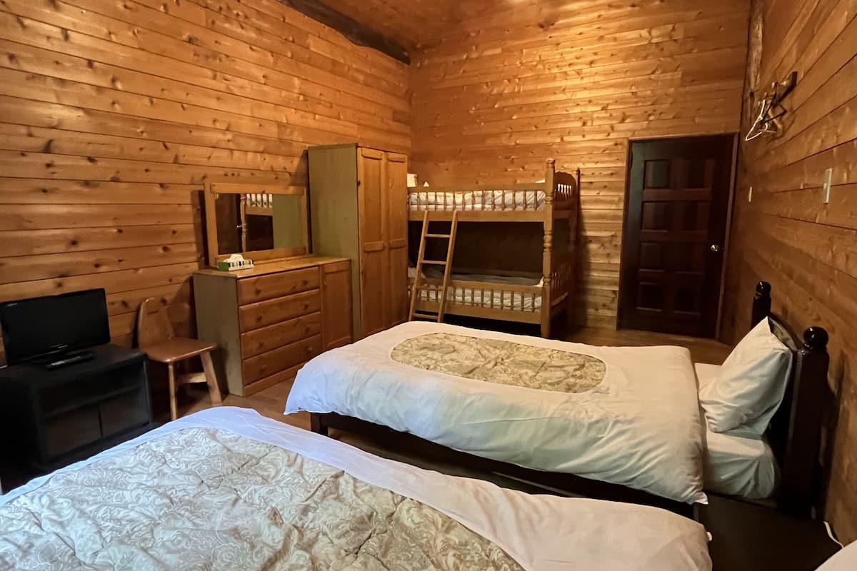 A wooden cabin room with two beds, a desk, a chair, a ladder, and a television.