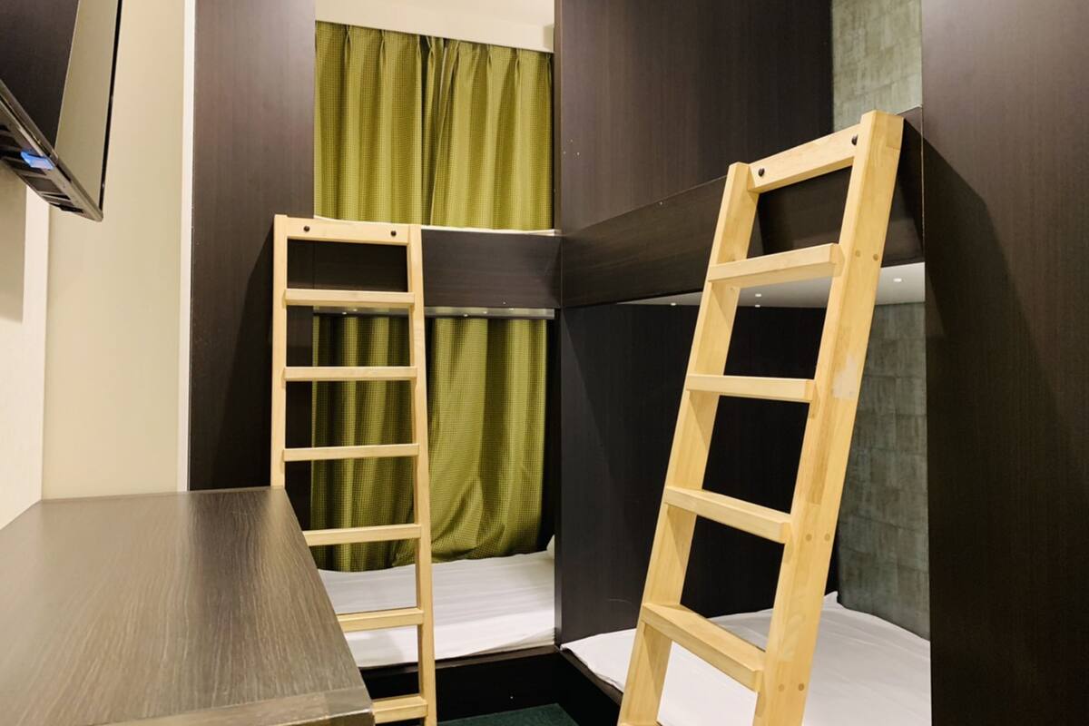 A small room with a bunk bed, a wooden ladder, a table, and a TV mounted on the wall.