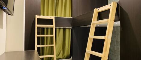 A small room with a bunk bed, a wooden ladder, a table, and a TV mounted on the wall.