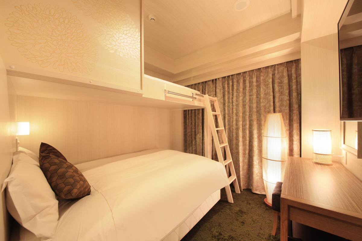 A hotel room with a bunk bed, a desk, and a ladder.