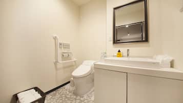 Une salle de bain moderne avec des toilettes blanches, un lavabo surmonté d’un miroir et une poubelle.