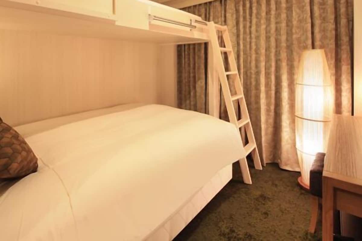 Una habitación de hotel con literas, un escritorio con silla, una lámpara y una ventana con cortinas.