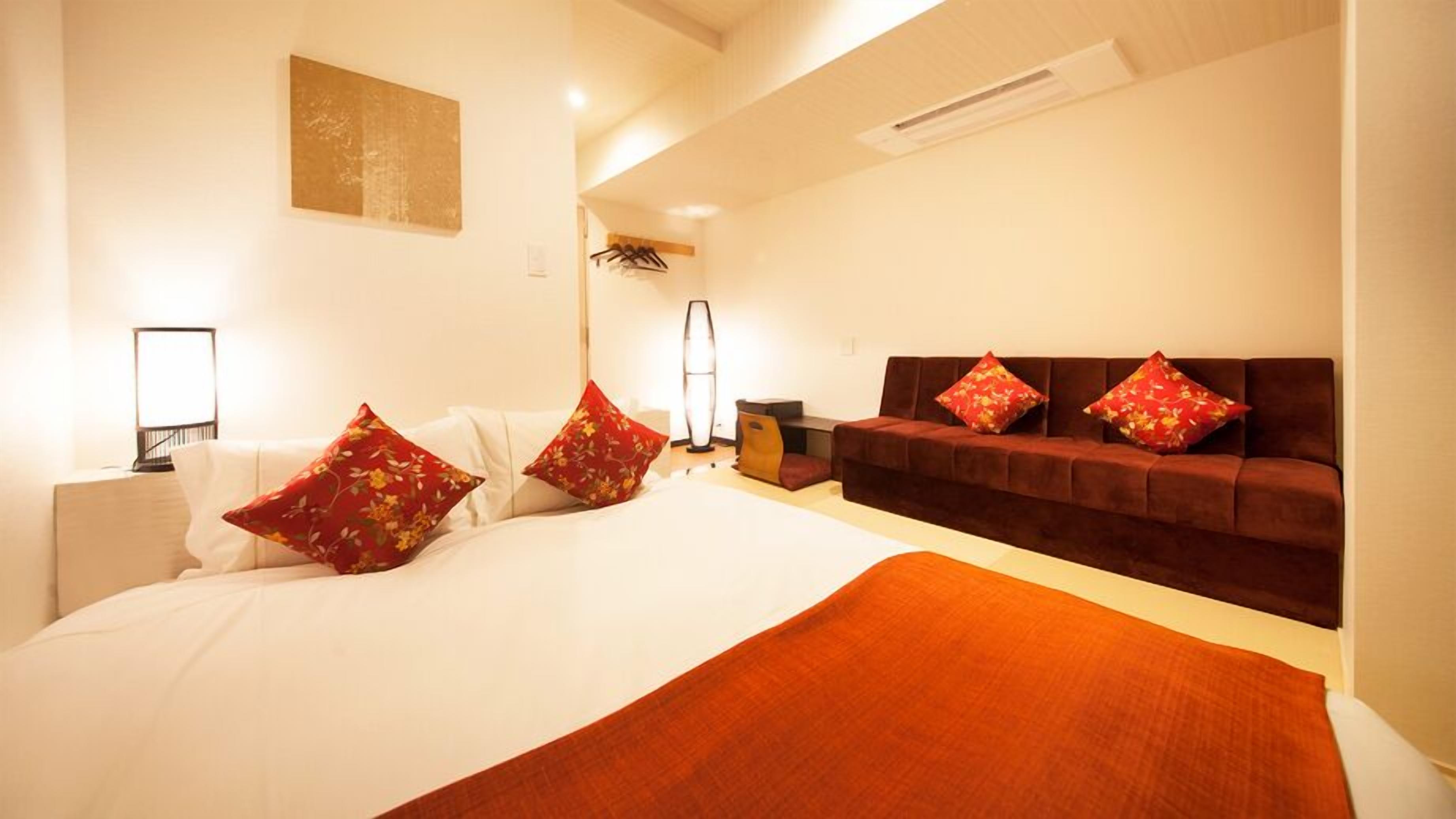 A hotel room with a large bed, a sofa, a desk, and a lamp.