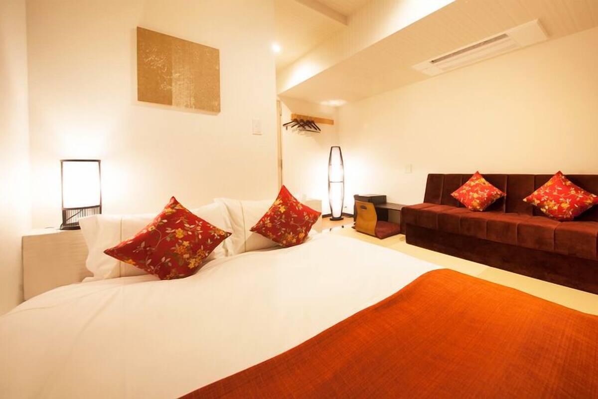 A hotel room with a large bed, a sofa, a desk, and a lamp.