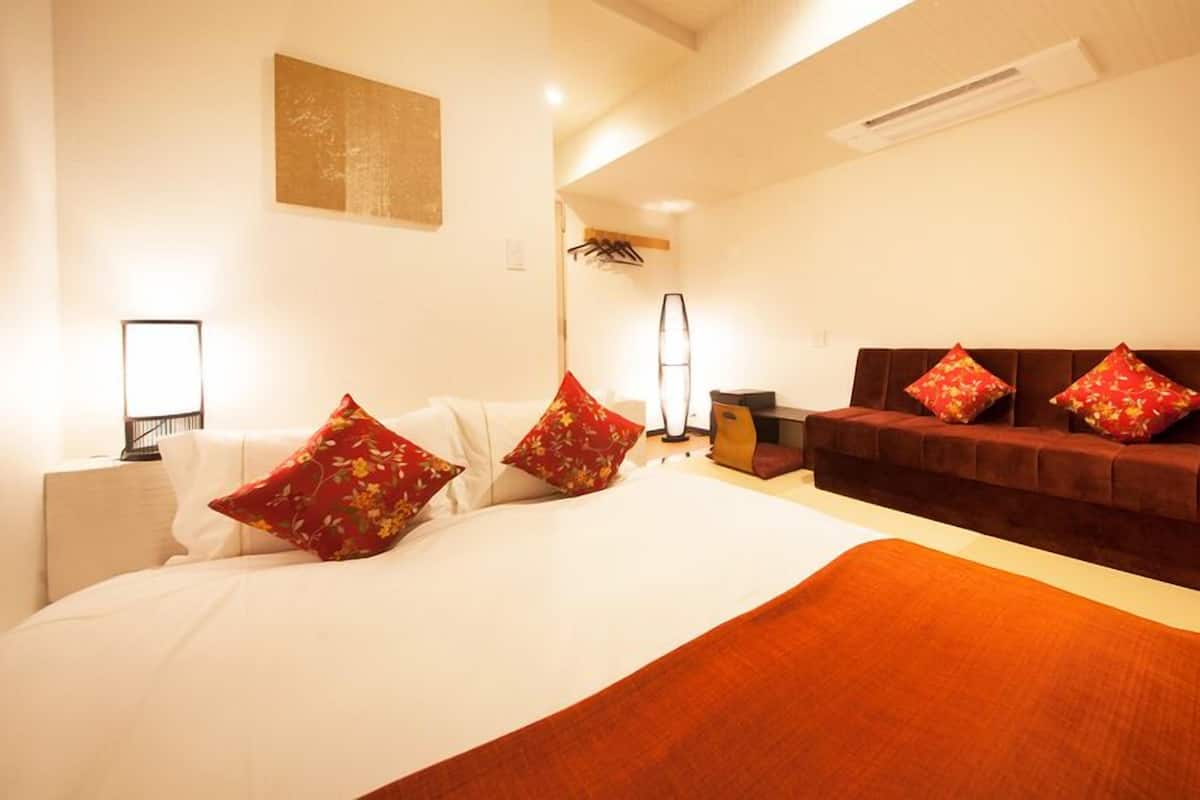 A hotel room with a large bed, a sofa, a desk, and a lamp.