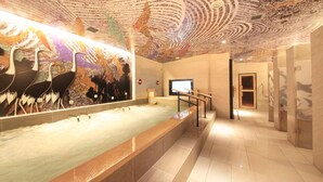 A modern bathroom with a large bathtub, a decorative ceiling mural, and a marble floor.