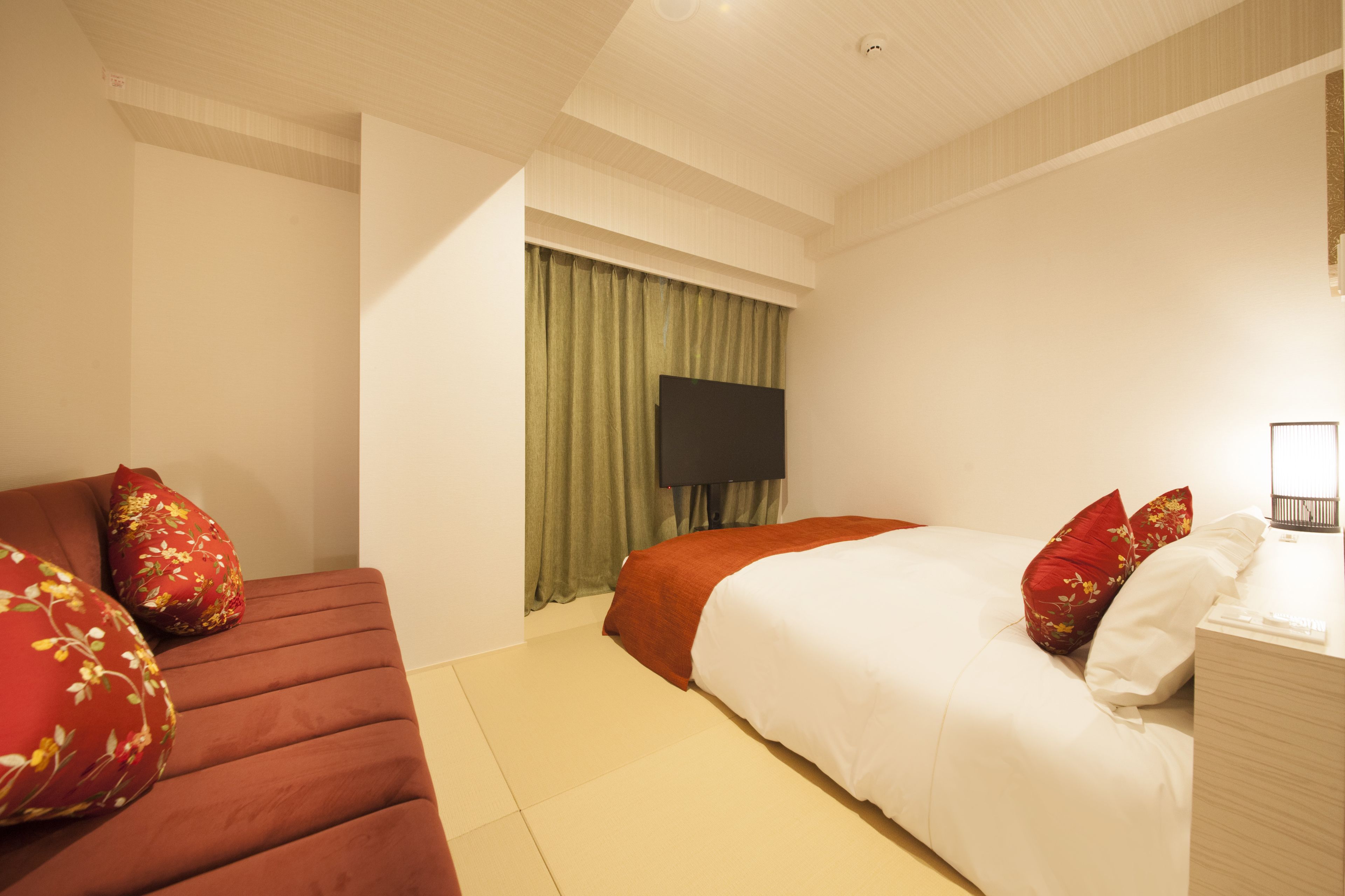 A hotel room with a bed, a sofa, a TV, and a bedside table.