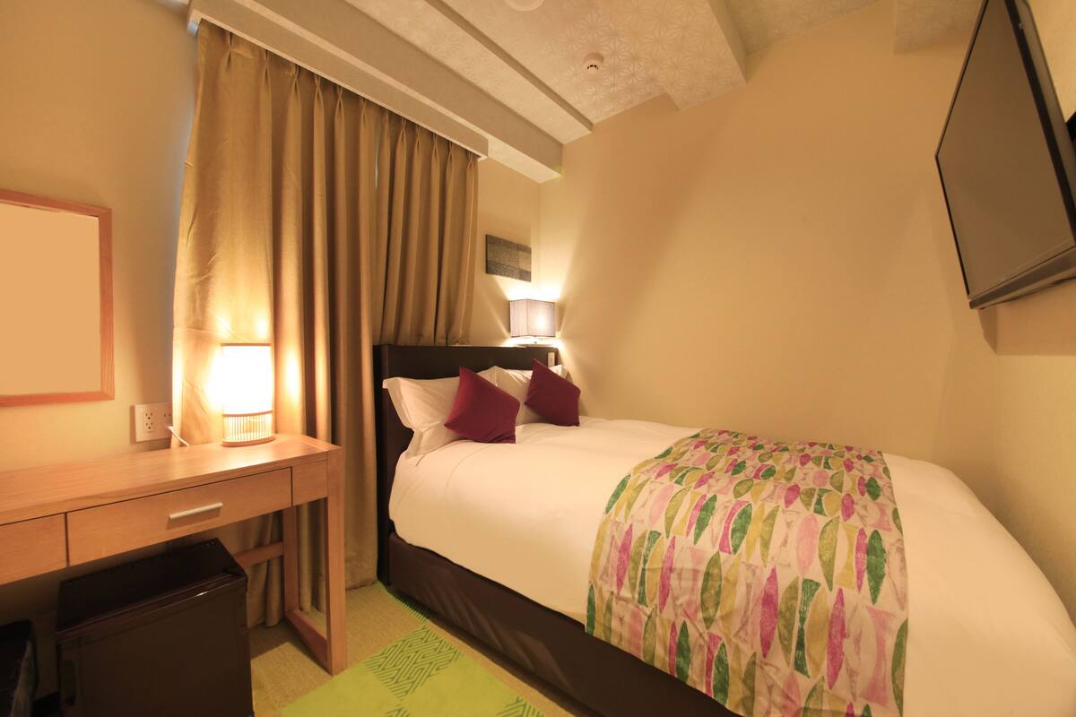 A hotel room with a bed, a desk, a lamp, and a television.